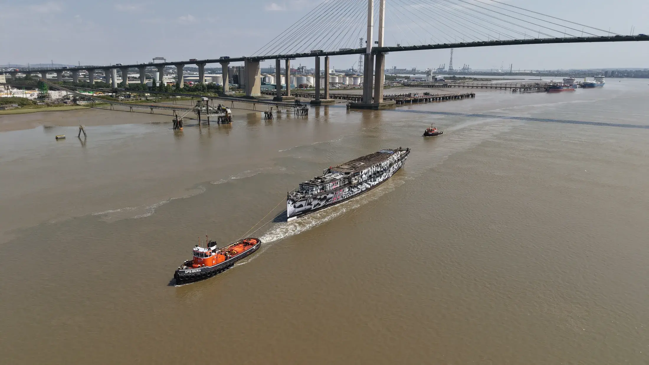 Aerial photograph of HMS President 1918 under tow passing beneath the Queen Elizabeth II Bridge at the Dartford Crossing.
