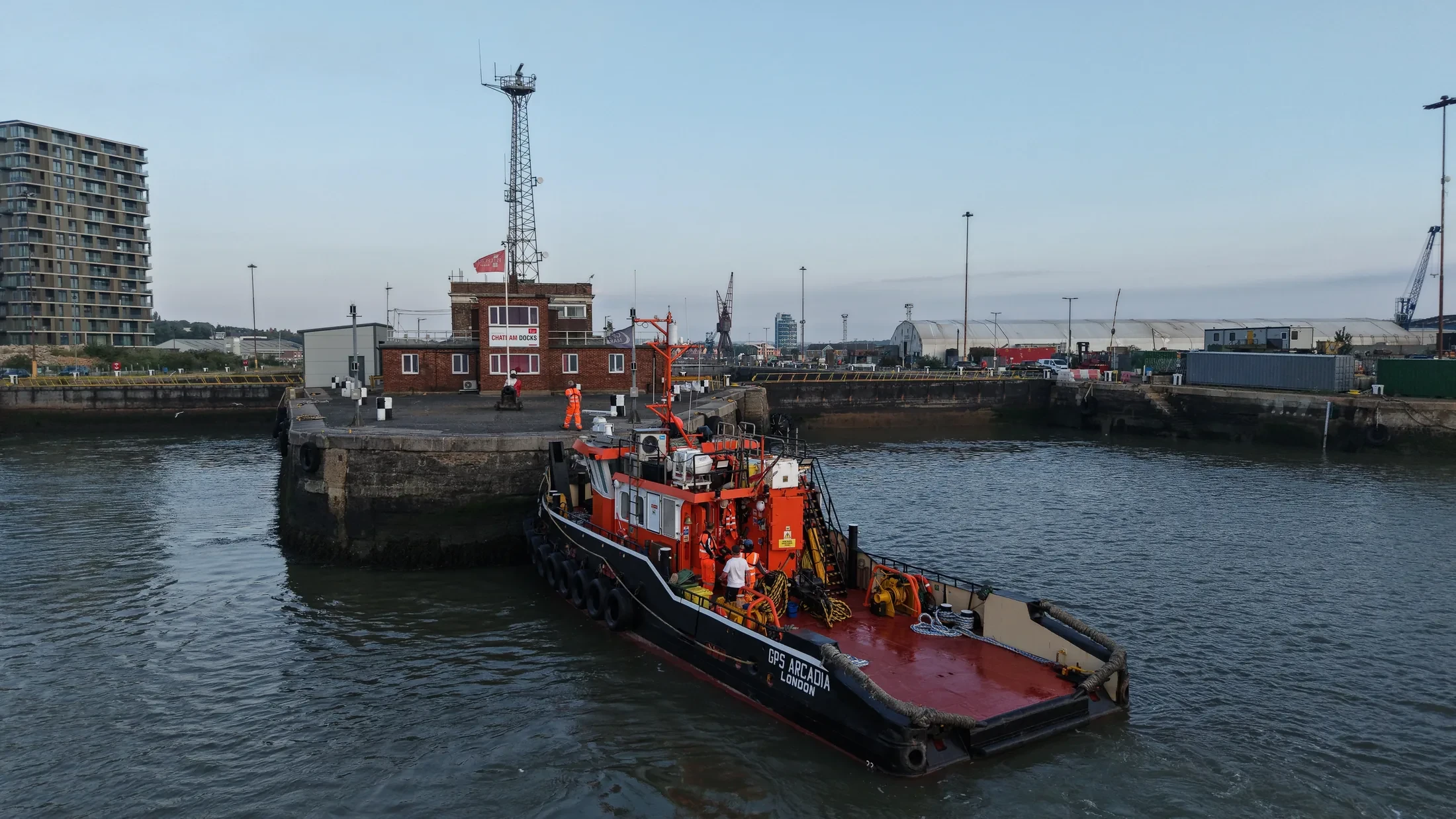 Overhead aerial photograph of a tug held against the dockyard wall at Chatham while crew transfer ashore