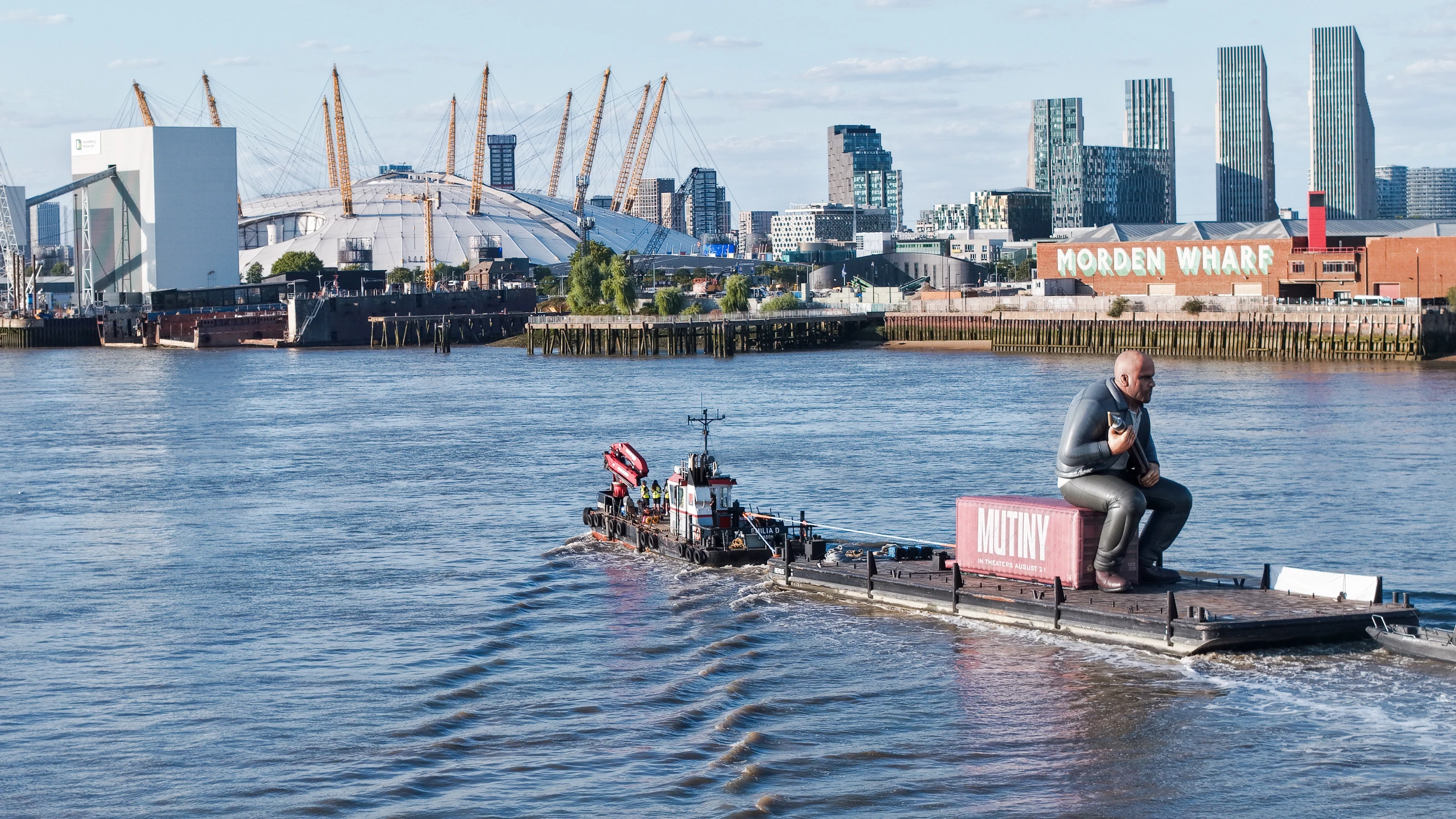 The Mutiny brand activation being towed past Morden Wharf on the Greenwich Peninsula, with the O2 arena beyond.