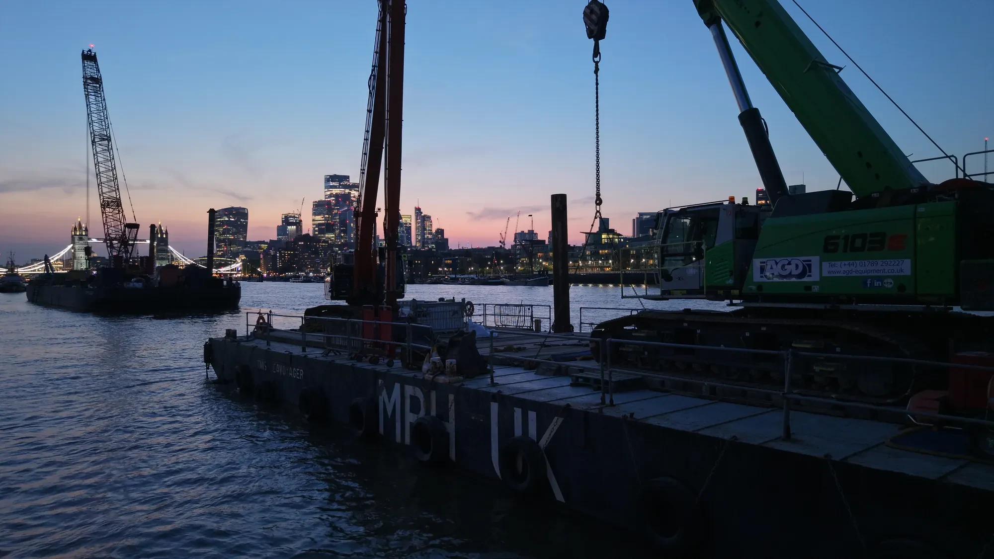 The AGD Equipment crane aboard the TMS Seavoyager pontoon at sunset on the Thames, City of London behind