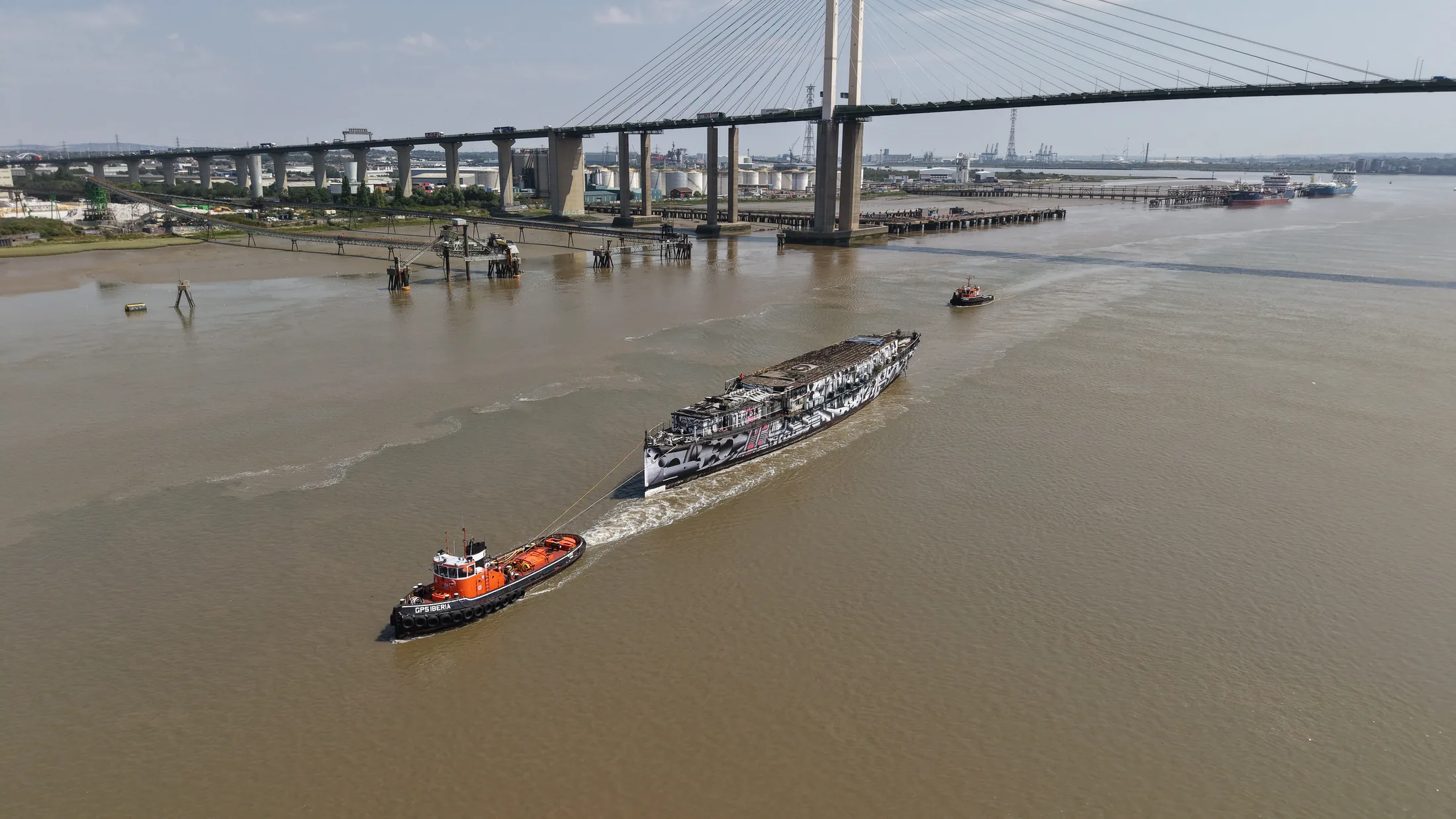 Aerial photograph of HMS President 1918 under tow passing beneath the Queen Elizabeth II Bridge at the Dartford Crossing.