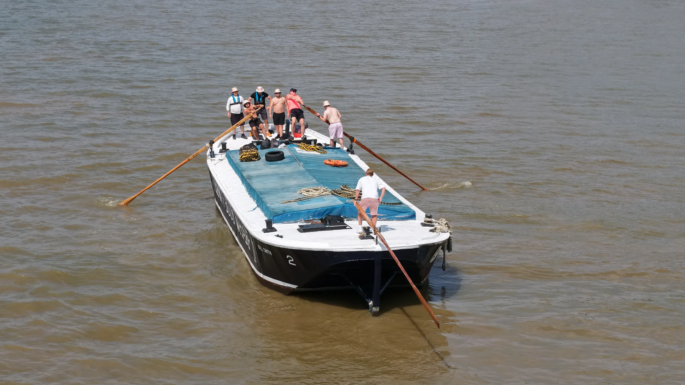 Aerial photograph of a Thames barge under oars during the race, with crew members working long sweeps over each side of the hull.