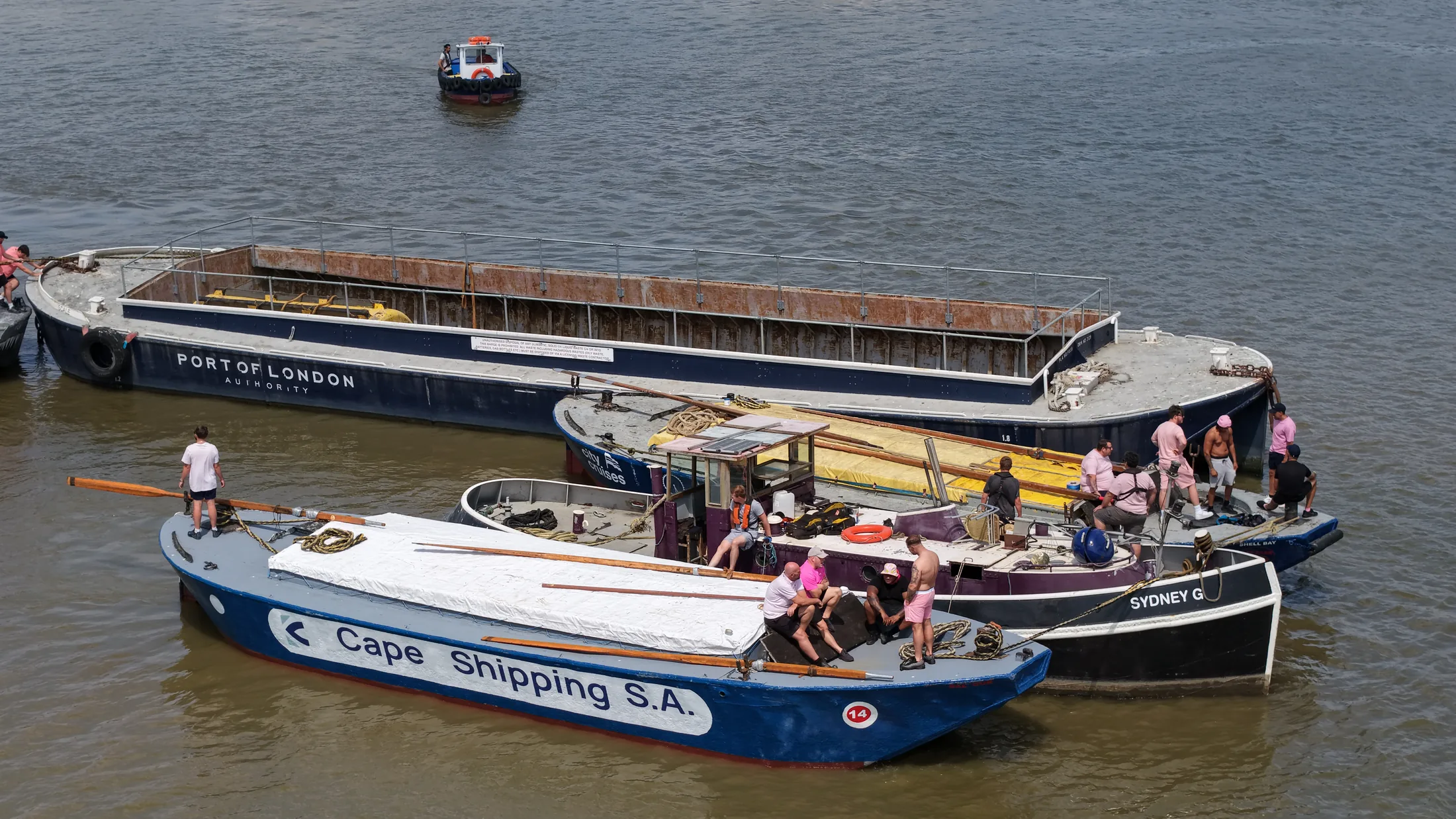 Aerial photograph of a barge crew aboard a blue Thames lighter lettered Cape Shipping S.A., with a Port of London Authority barge alongside.