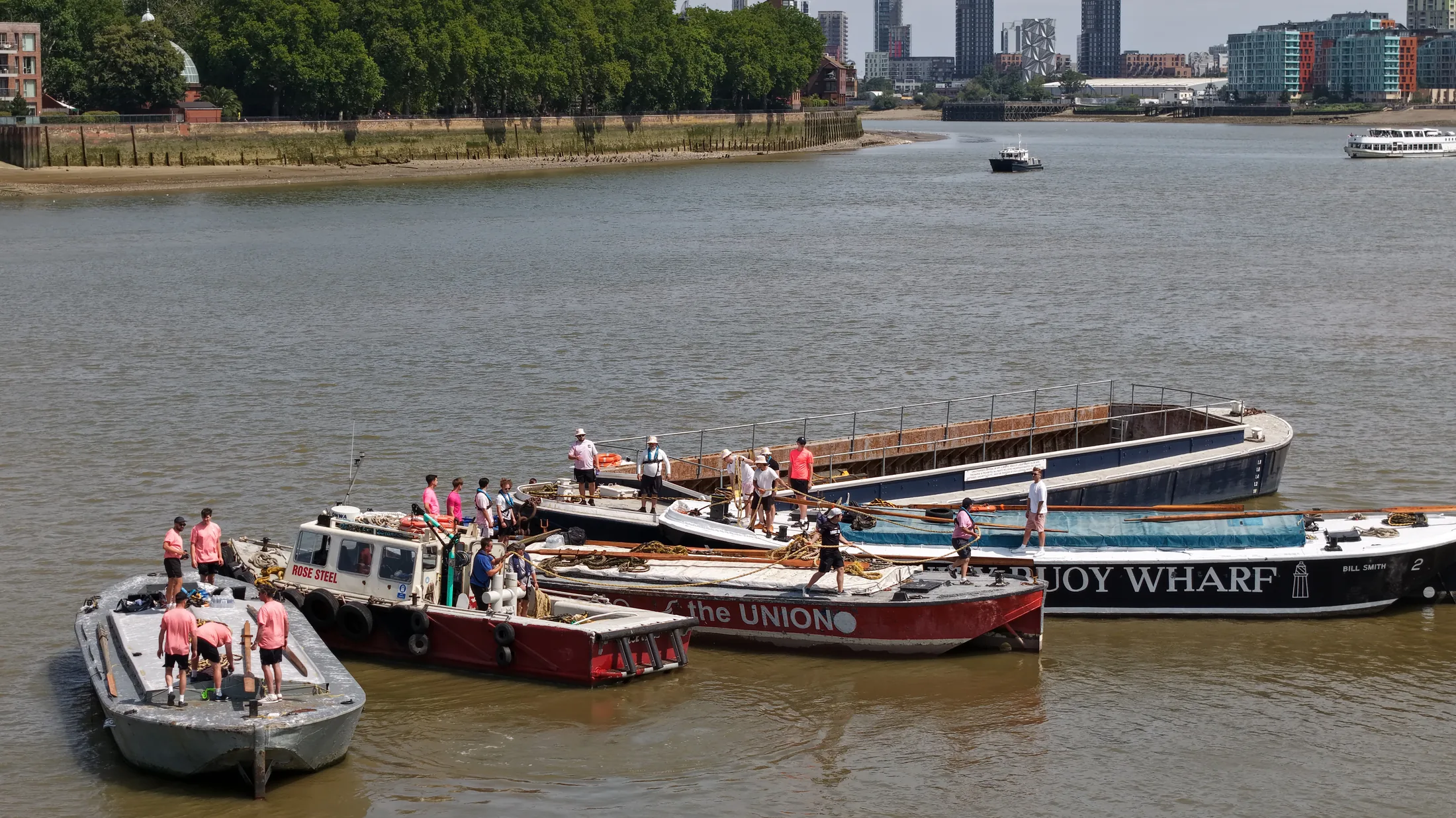 Aerial photograph of barge crews on deck preparing their oars and gear before the race, with a Trinity Buoy Wharf barge alongside.