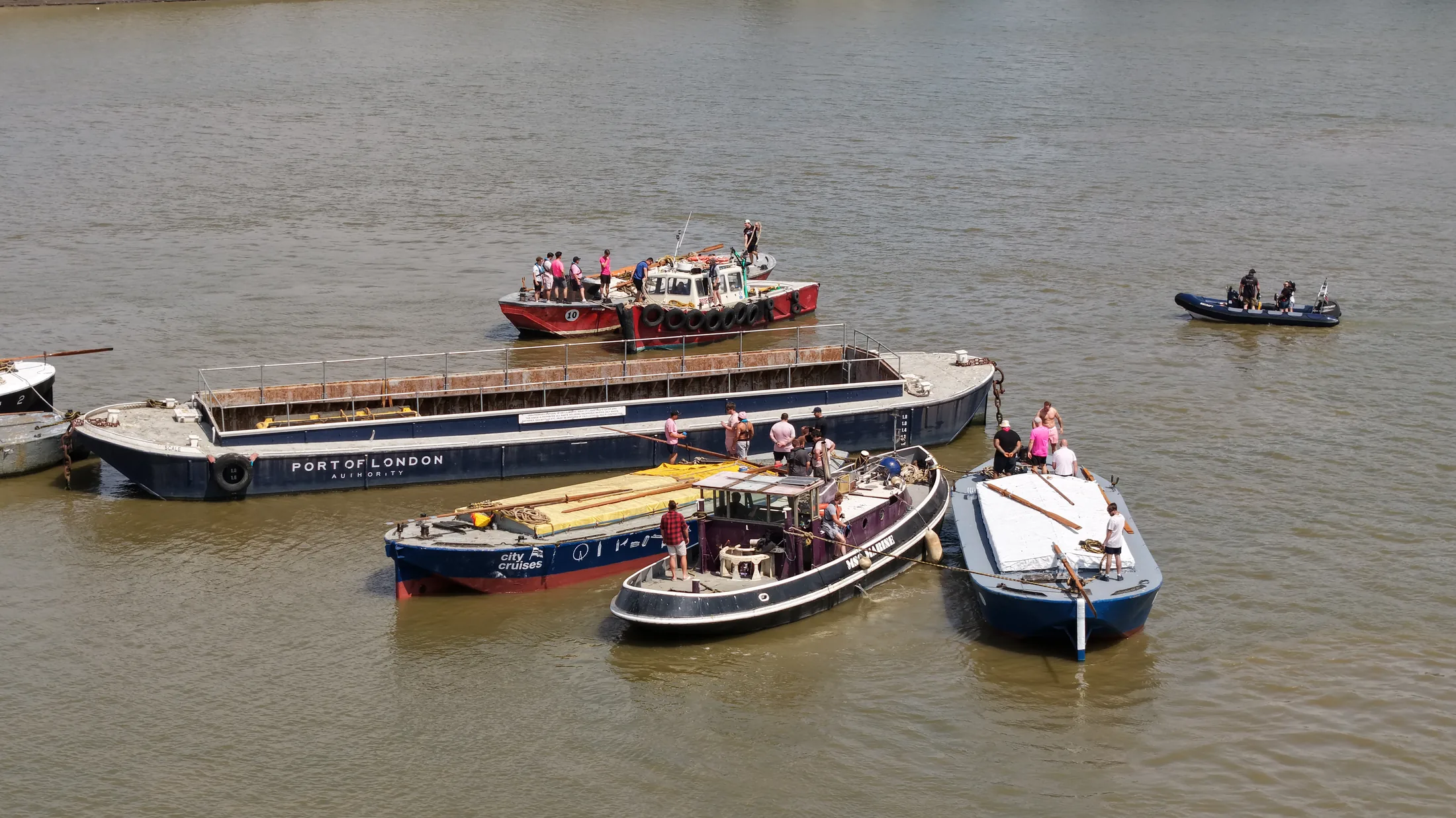 Aerial photograph of a Port of London Authority barge with crew aboard, rafted alongside an attending tug on the Thames at Greenwich.
