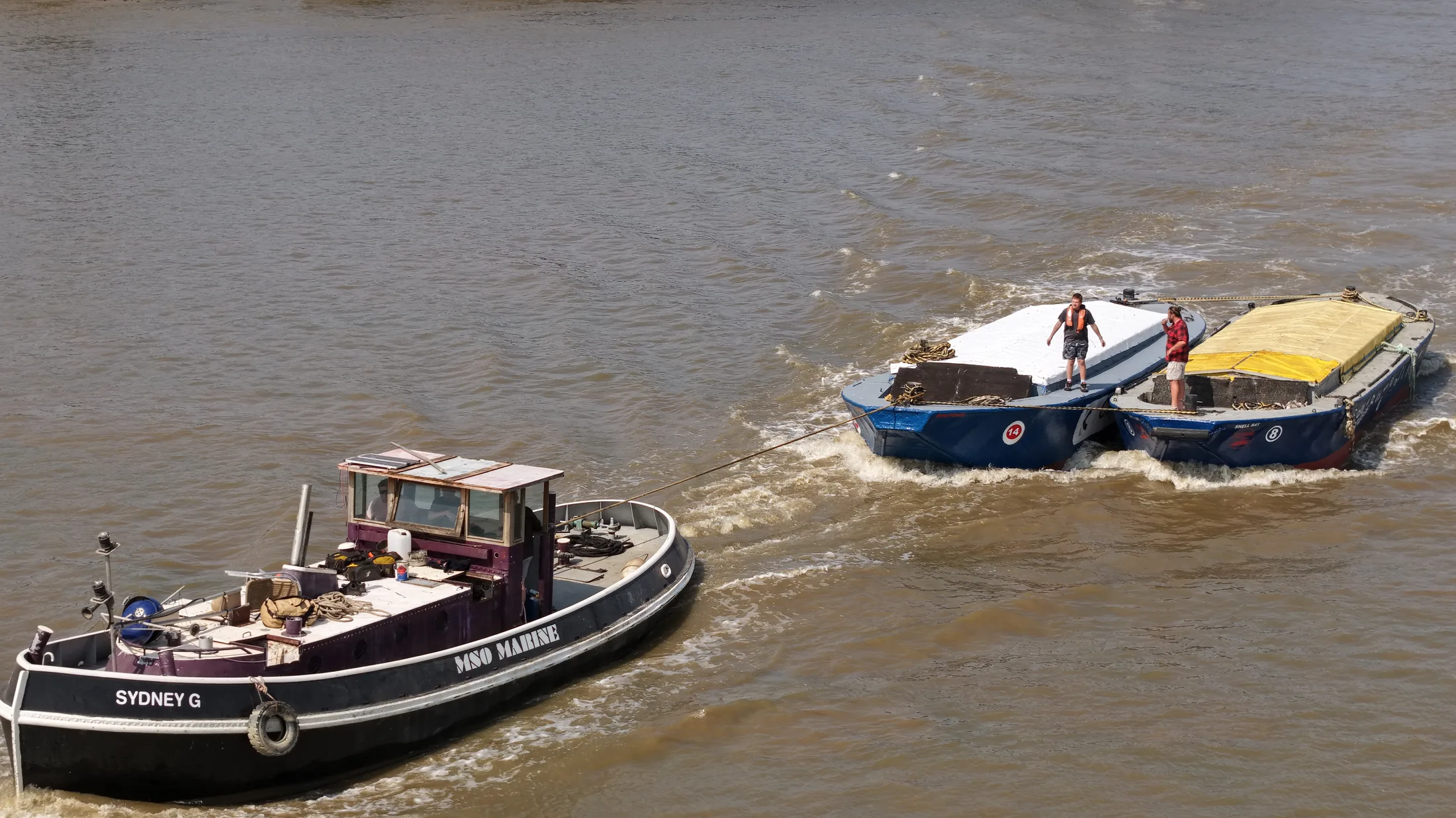 Aerial photograph of the tug Sydney G towing two Thames barges with crew aboard on the River Thames.