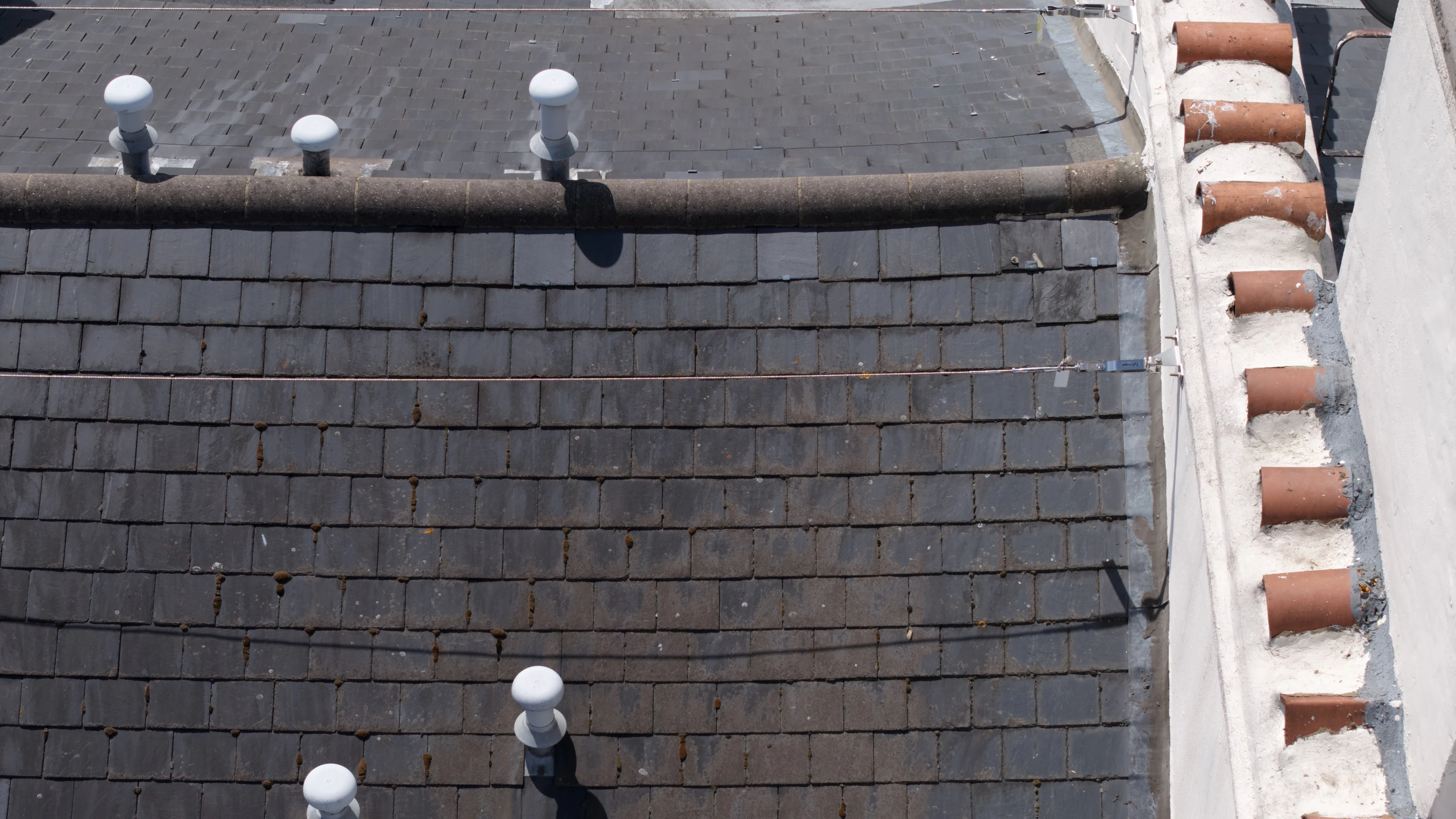 Close aerial detail of a chimney stack, flaunching and chimney pots against the slate ridge of a terrace roof.