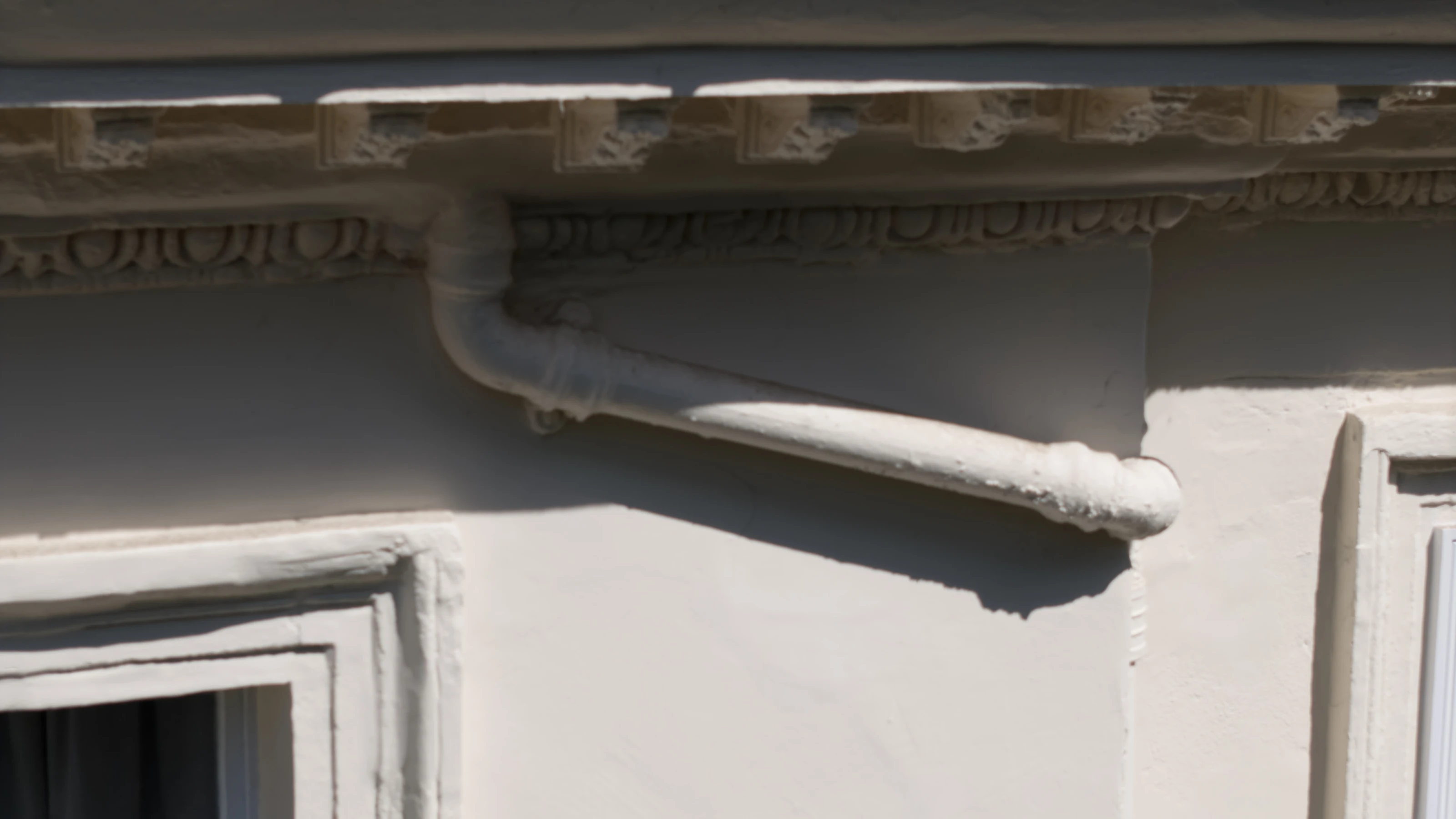 Close drone inspection detail of a moulded cornice and cast iron rainwater hopper and downpipe on a stucco building.