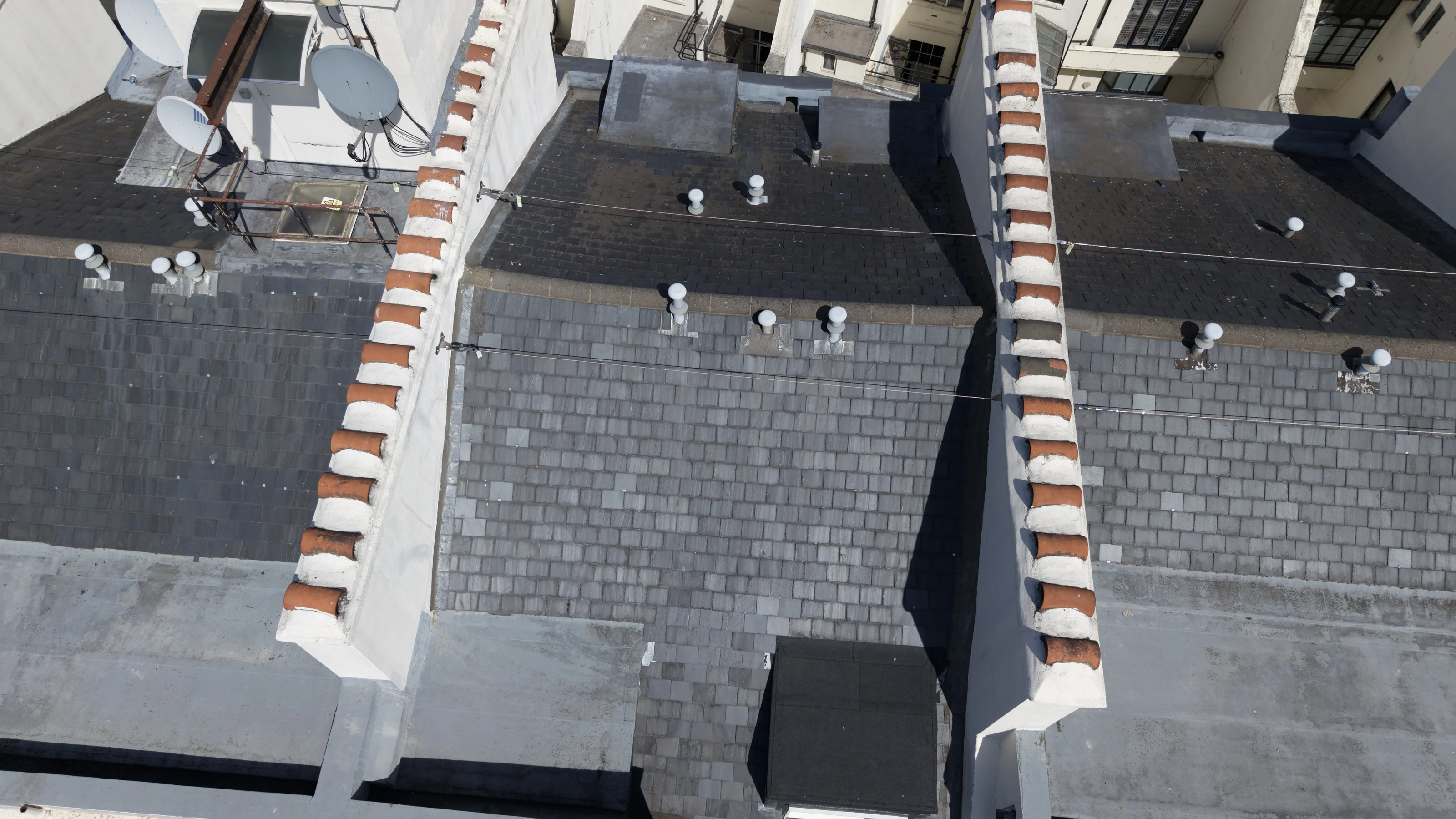 Aerial view along a terrace roofline during a building fabric survey, with the run of chimney stacks and slate pitches recorded in sequence