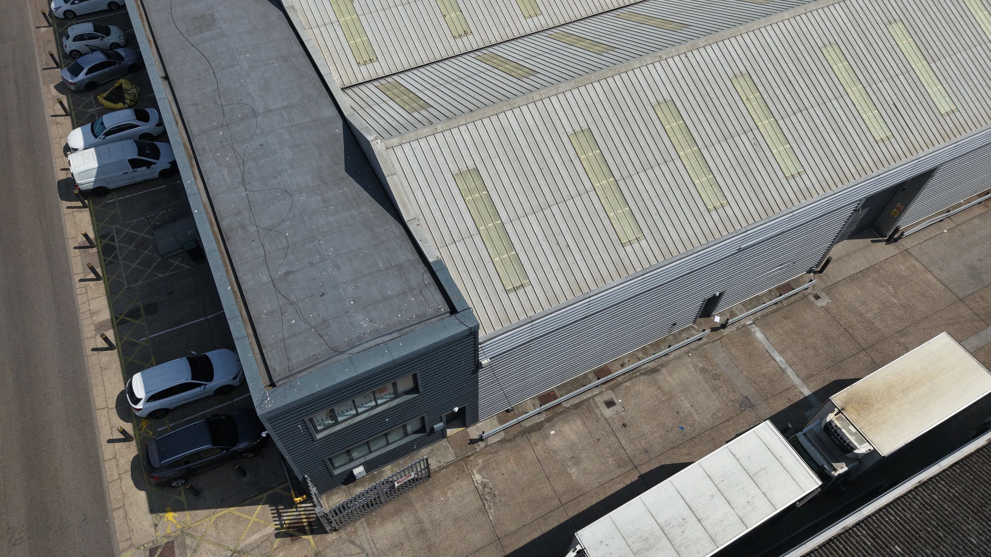 Oblique aerial view of an industrial unit during a drone roof condition survey, showing the roof, elevation and service yard together