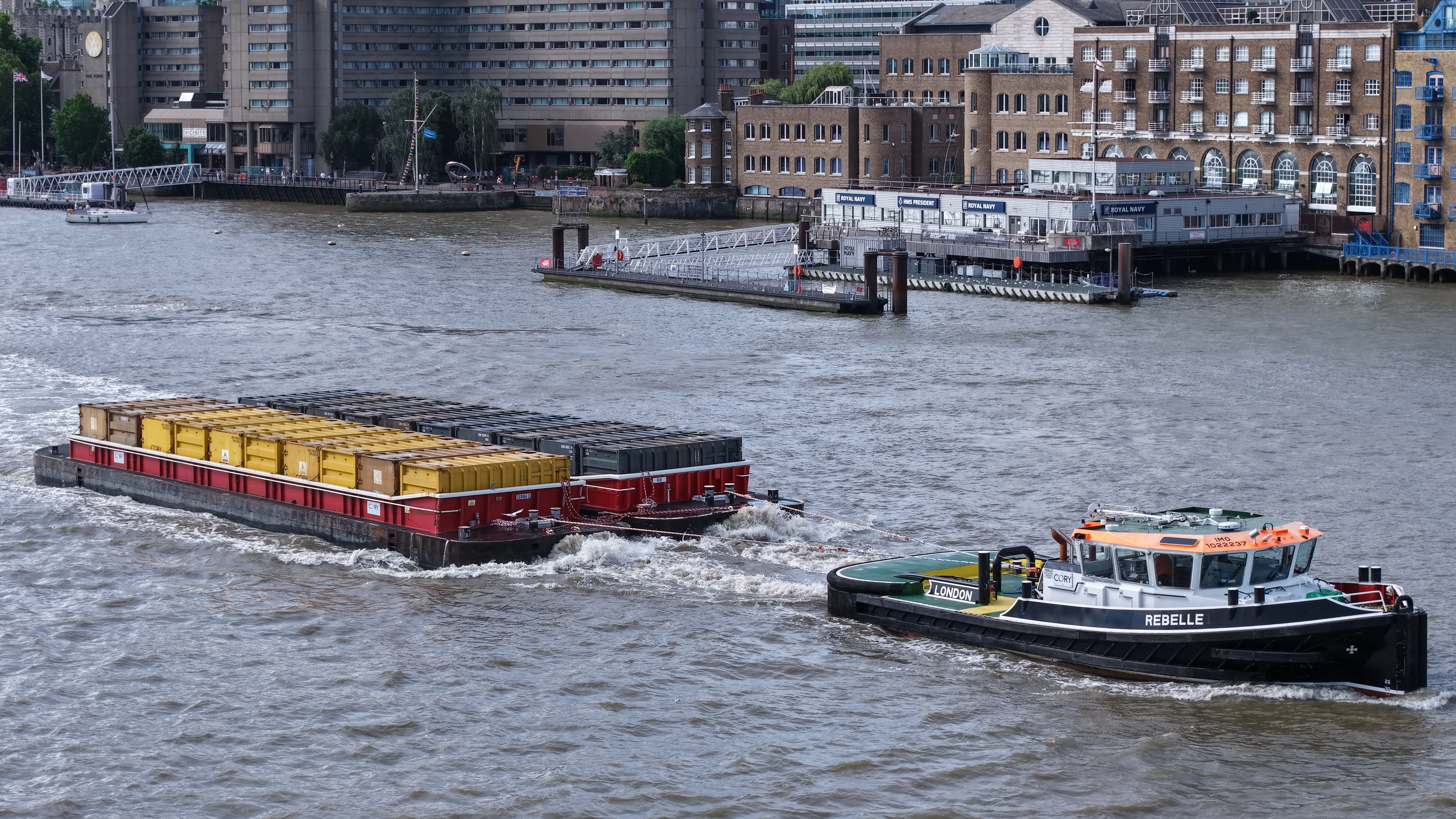 The Cory tug Rebelle towing the container barge Gemma D on the River Thames, tow line taut and the loaded containers astern