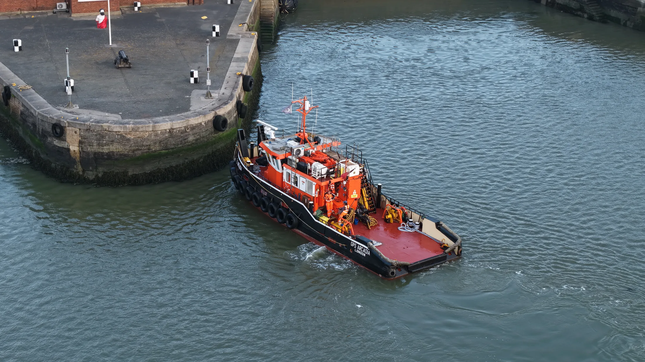 The tug making her approach to the quay wall at Chatham Docks on the River Medway, seen from above.