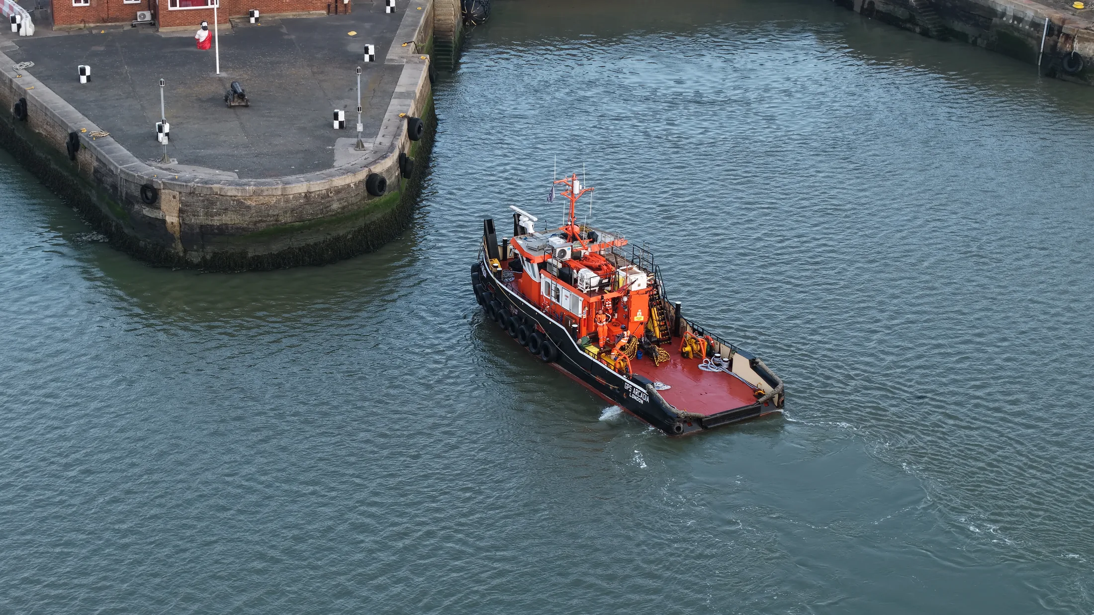Aerial photograph of a tug approaching the dockyard wall at Chatham in early morning light for a crew transfer.