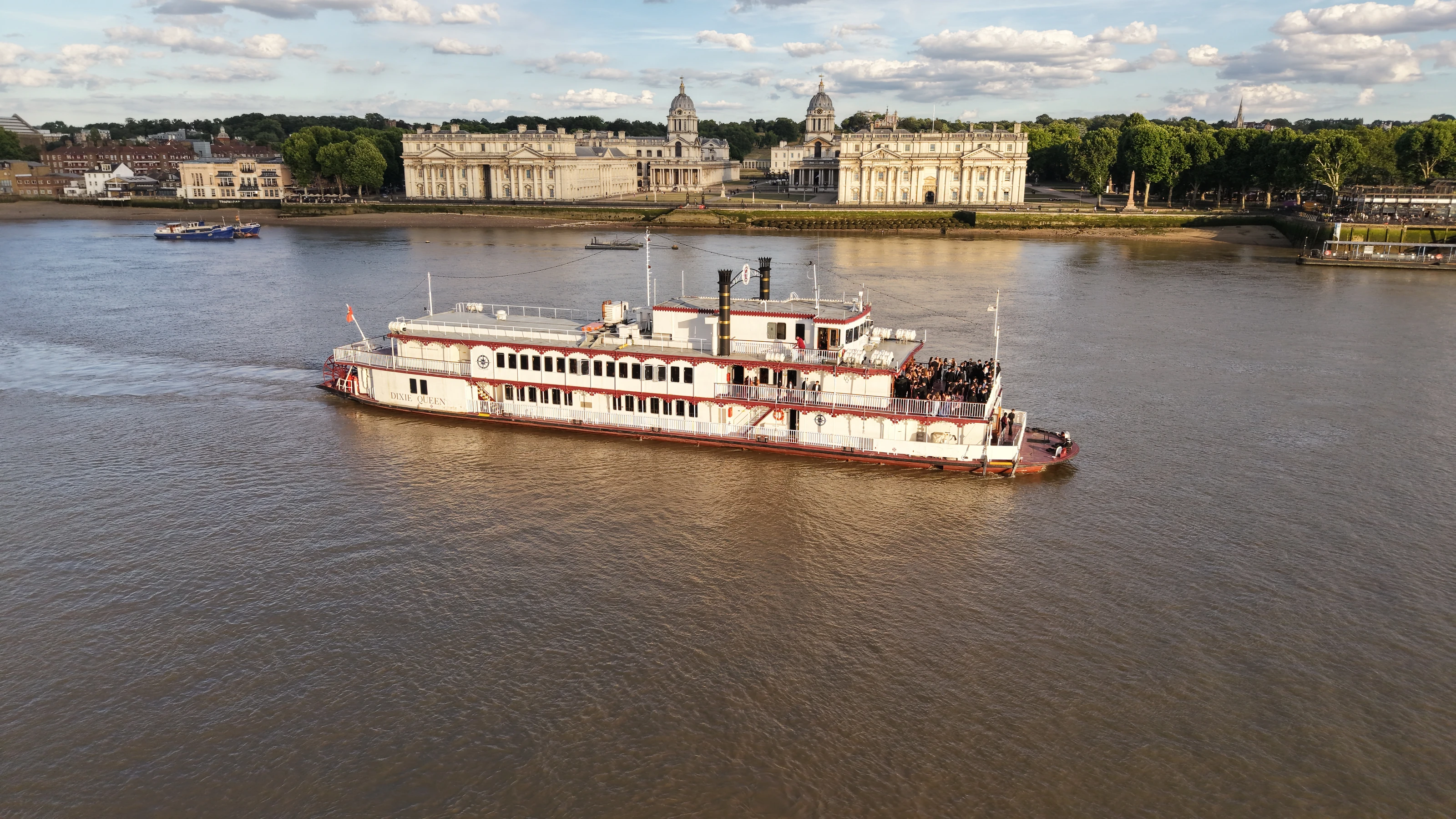 Aerial view of the Dixie Queen under way on the tidal Thames at Greenwich in low evening sun.