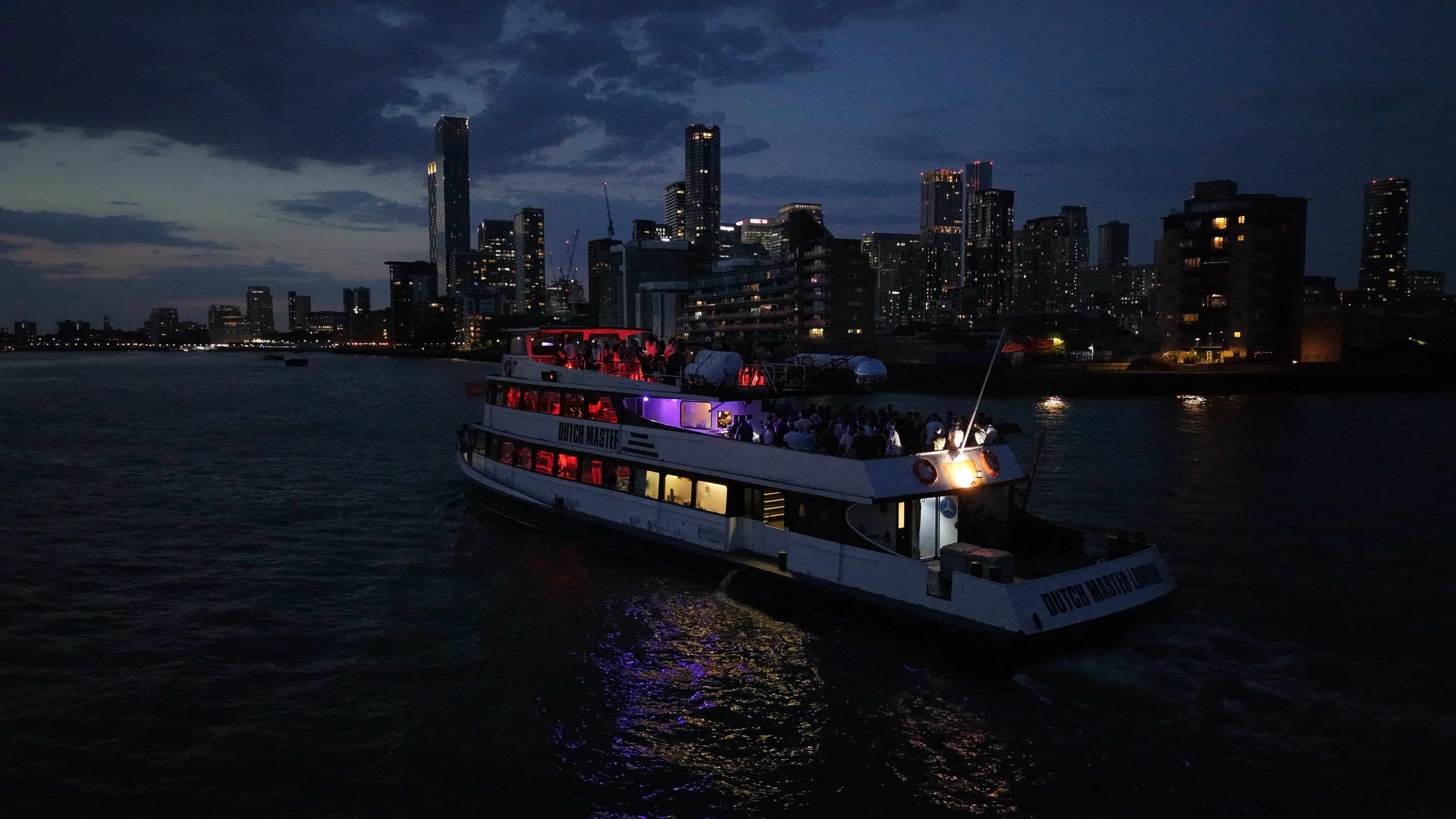 The Dutch Master illuminated at night on the Thames, colour from the interior decks reflected across the water