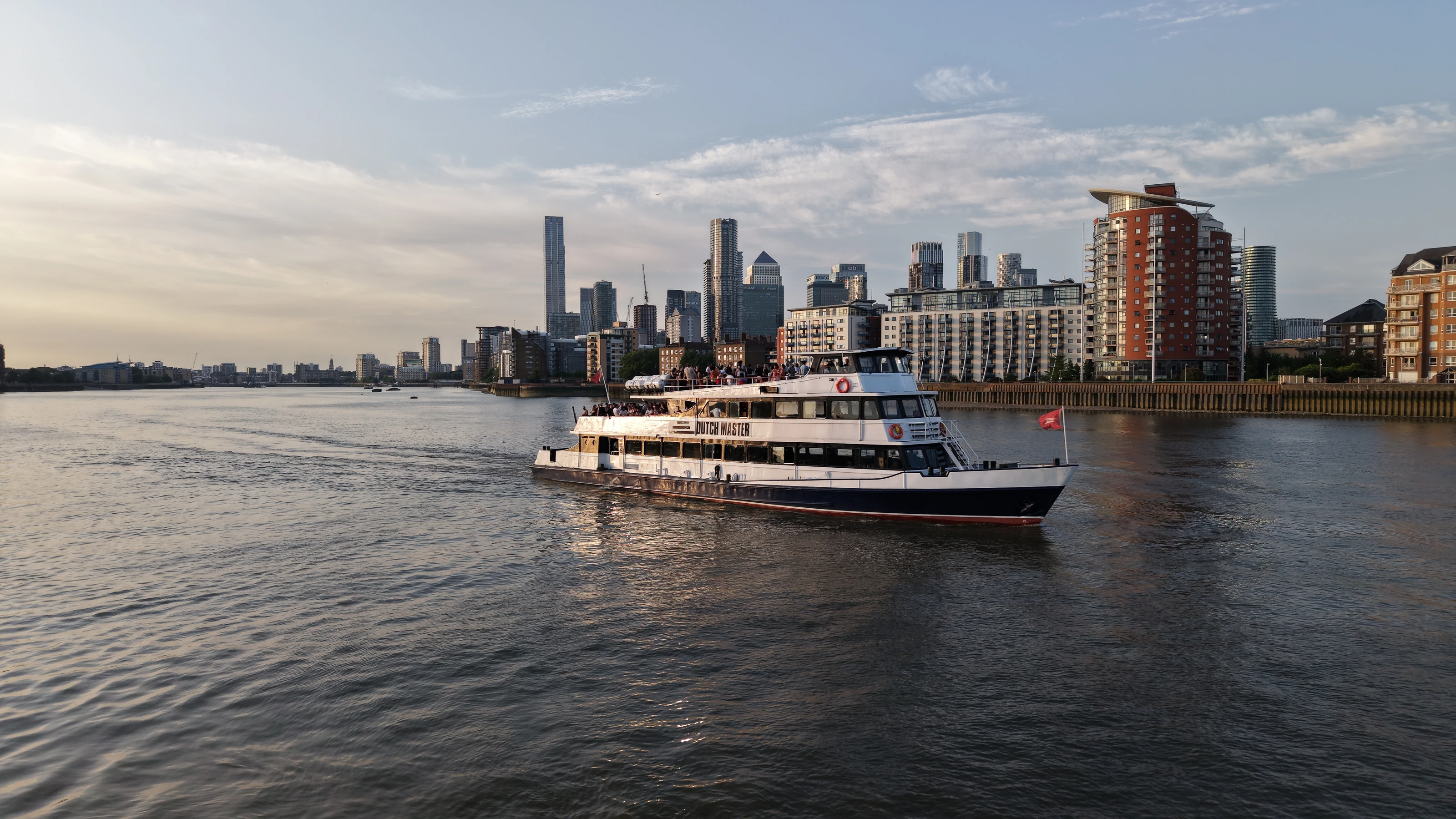 The Dutch Master on the tidal Thames in low evening light with the Canary Wharf towers on the skyline behind