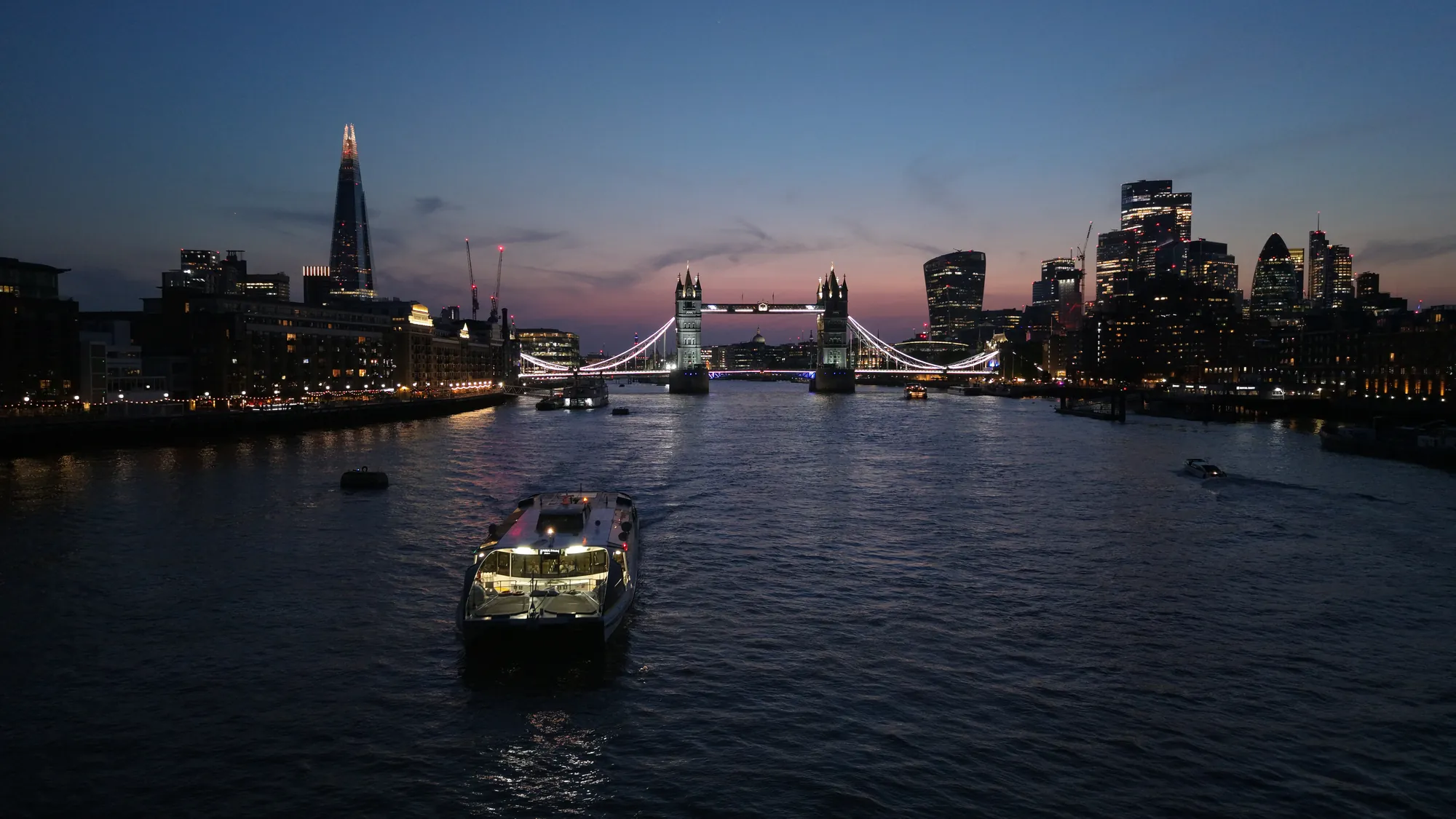 Blue hour aerial photograph of Tower Bridge and the illuminated City of London skyline.