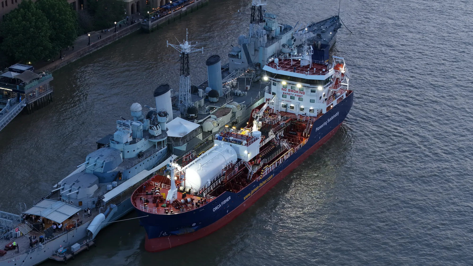 Overhead aerial photograph of the Orca Fisher tanker moored alongside HMS Belfast on the Thames at night