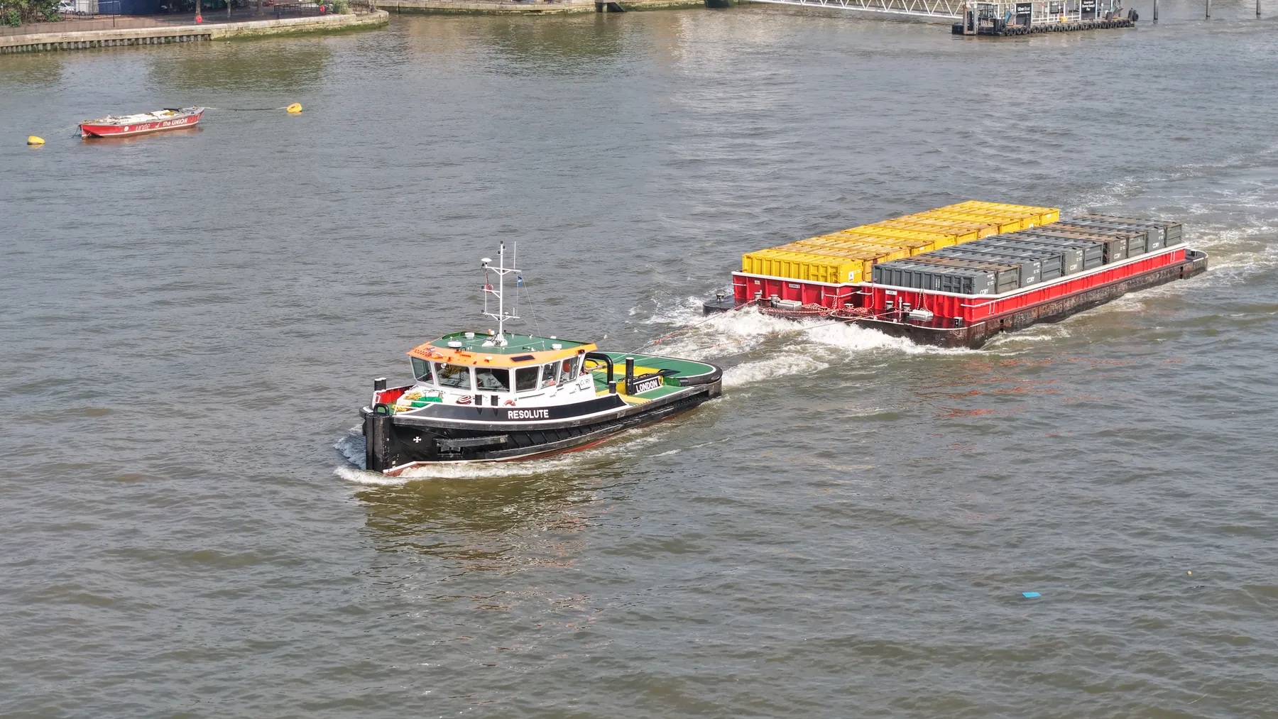 Cory tug Resolute towing a loaded container barge up the Thames, captured by drone